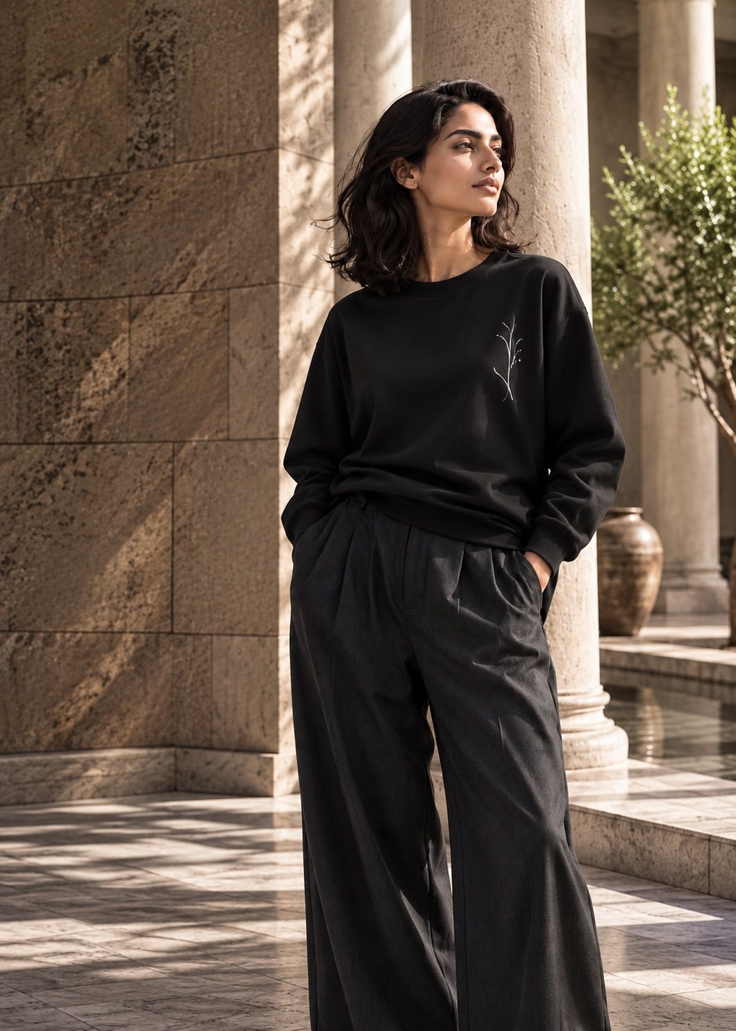 A woman in a black sweatshirt with a fine branch print, standing by stone columns